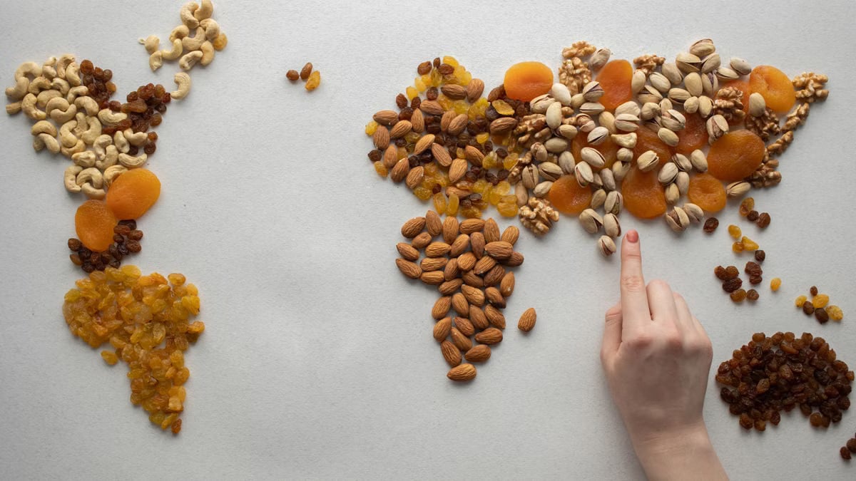 Top view of crop anonymous person making world continents with various nuts and heap of dried fruits on white background